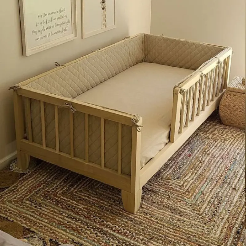 A toddler's wooden bed with a quilted bumper pad.