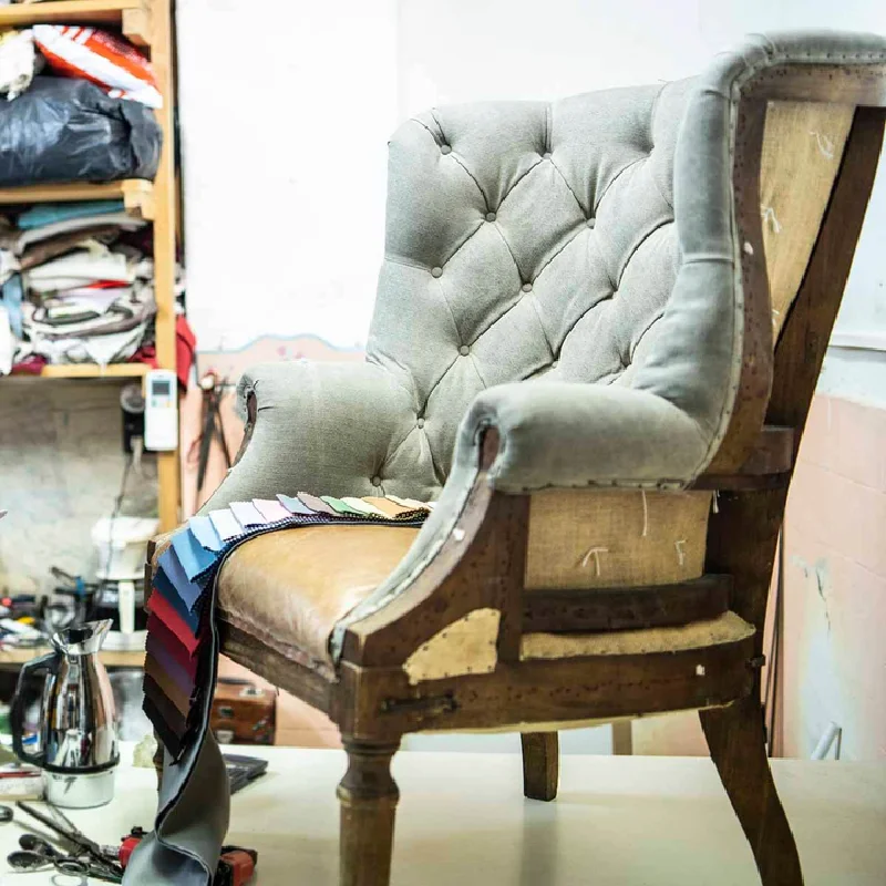 examines fabric swatches while working on a chair repair project