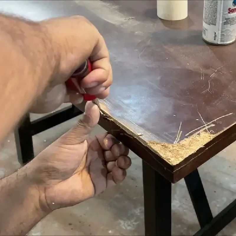 scrape off a damaged, chipped corner of a dark wooden table