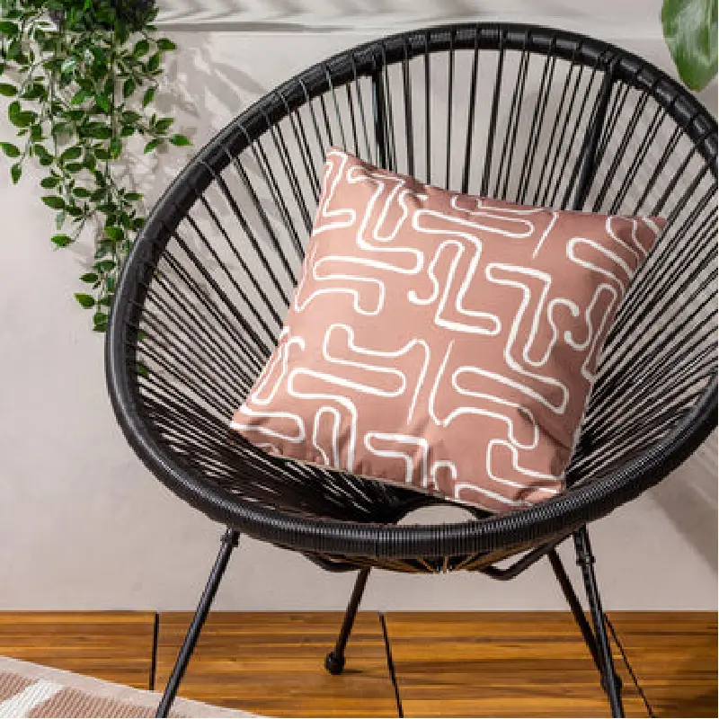 single salmon-pink outdoor cushion with a white abstract, maze-like pattern rests