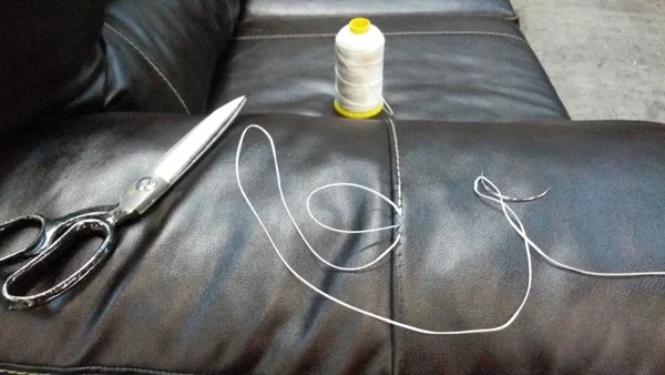 Scissors and thread on black leather couch for repair